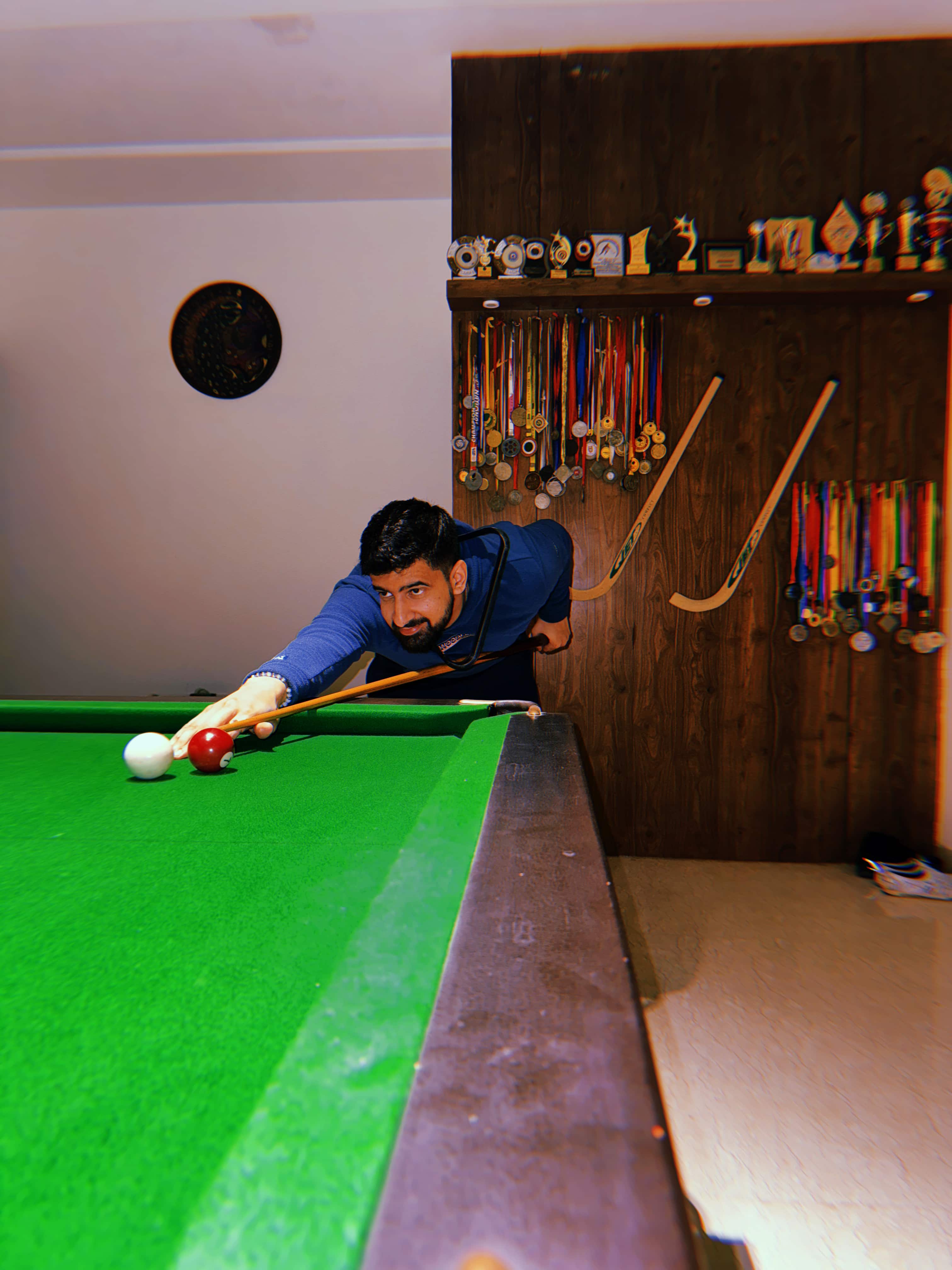 Parth playing pool at home in front of the medal wall
